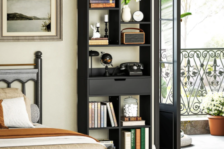 Black modern bookshelf beside bed near balcony, filled with books and décor accessories.