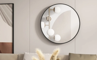 Round wall mirror with black frame reflecting light above beige sofa with cushions and pampas decor.