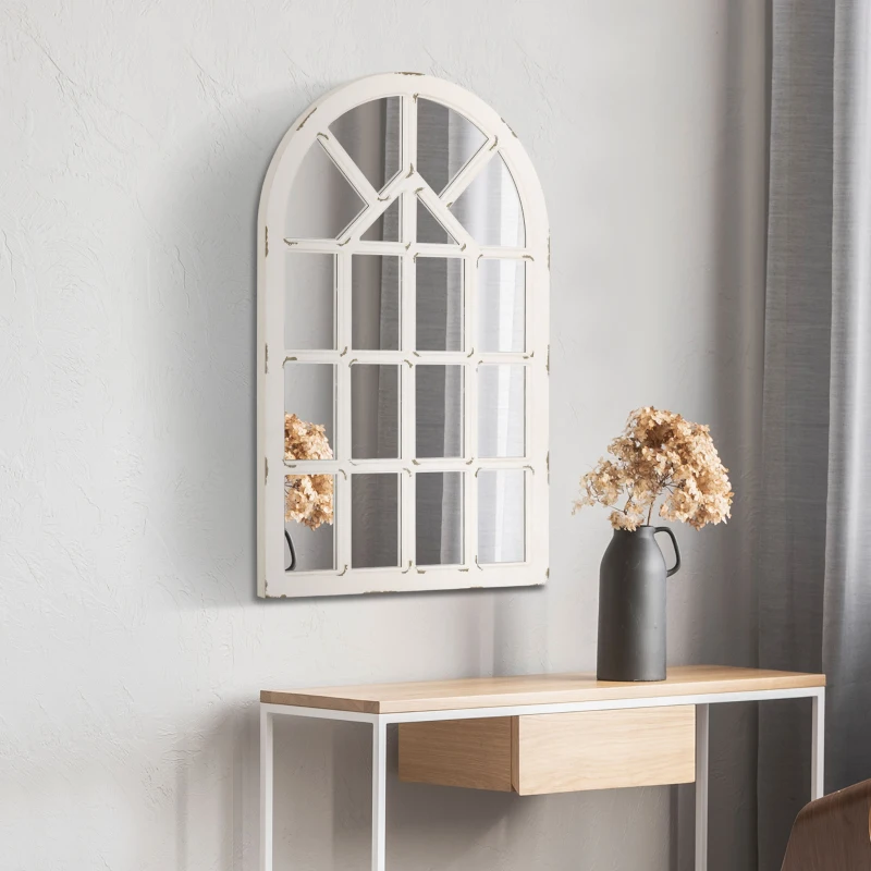 Tall arched wall mirror with windowpane design above console table decorated with flowers in a vase.