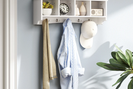 White wall-mounted coat rack with small cubby shelves holding clothes, hat, and decorative items.