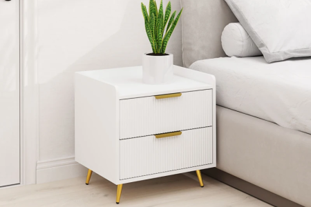 White modern bedside table with gold handles and legs, styled with green potted plant on top.