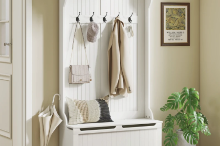 White hall tree with coat, bag, umbrella, cushion, and shelf décor in entryway.