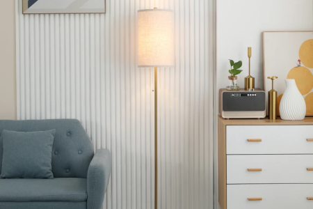 Modern gold floor lamp with fabric shade placed beside sofa and cabinet in a living room.