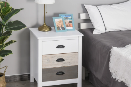 White bedside table with lamp, books, and photo frames in modern bedroom.