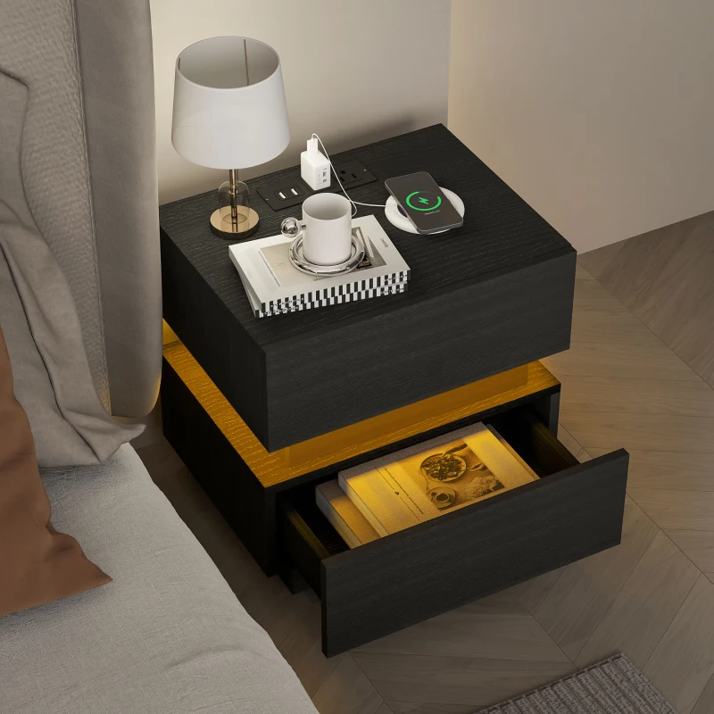 Black bedside table with lamp, open drawer, books, and phone charging on top.