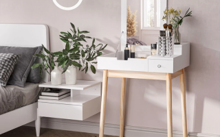 White dressing table with mirror, makeup items, and stool placed beside a bed in bright room.