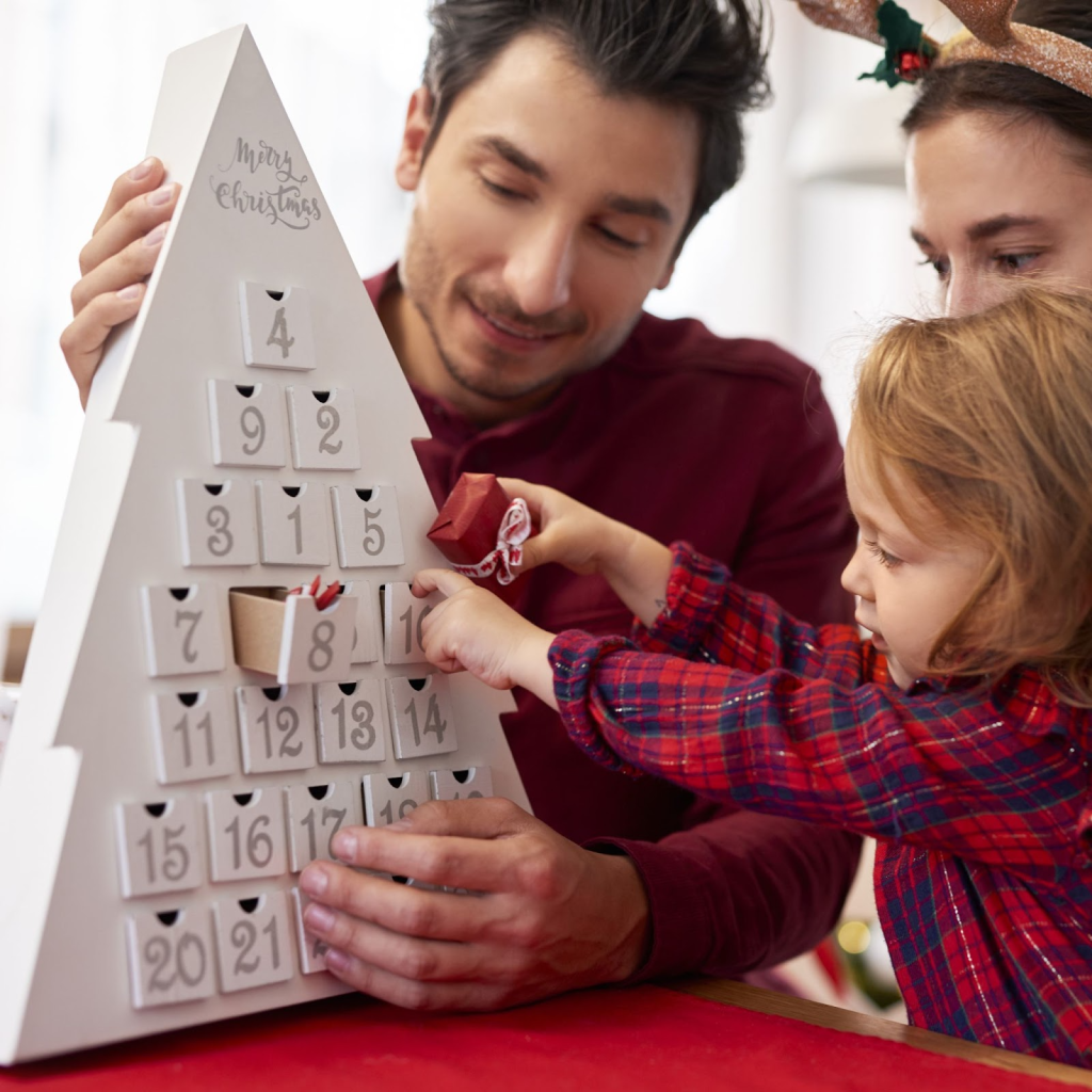 Family opening tree-shaped advent calendar with small gift boxes.