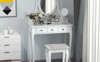 White vanity table with oval mirror decorated with flowers, brushes, and beauty products.
