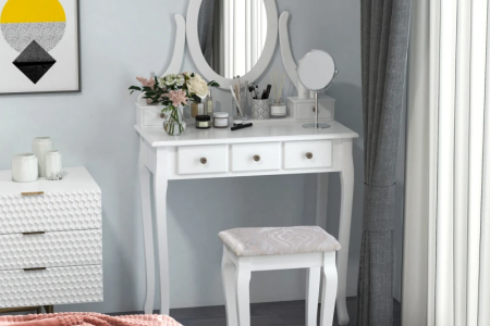 White vanity table with oval mirror decorated with flowers, brushes, and beauty products.
