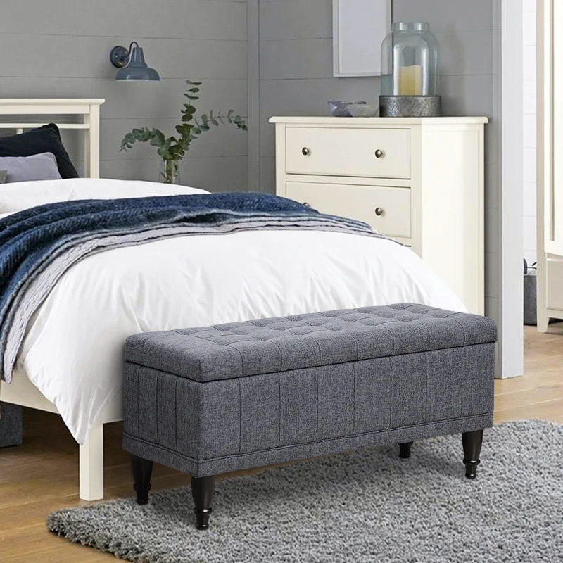 Gray tufted storage bench placed at foot of bed.