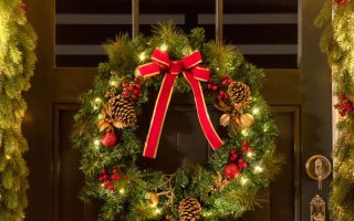 Christmas wreath with red bow and pinecones on dark door.