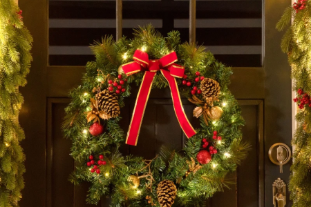 Christmas wreath with red bow and pinecones on dark door.