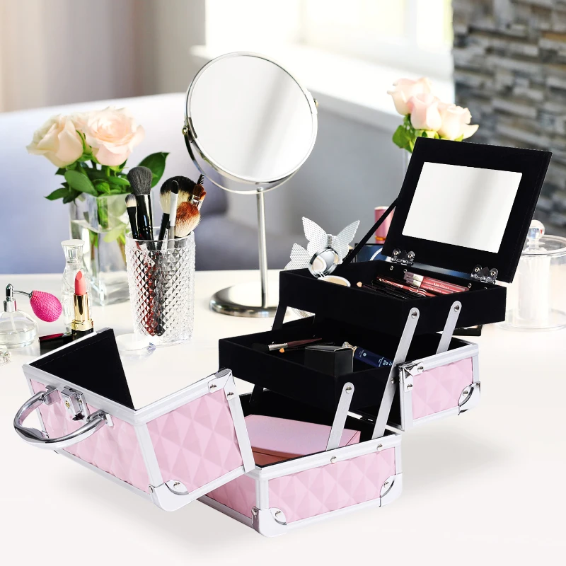 Pink three-tier makeup case open on vanity with brushes, mirror, and cosmetics arranged.