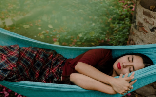 Woman sleeping on blue hammock outdoors surrounded by greenery.