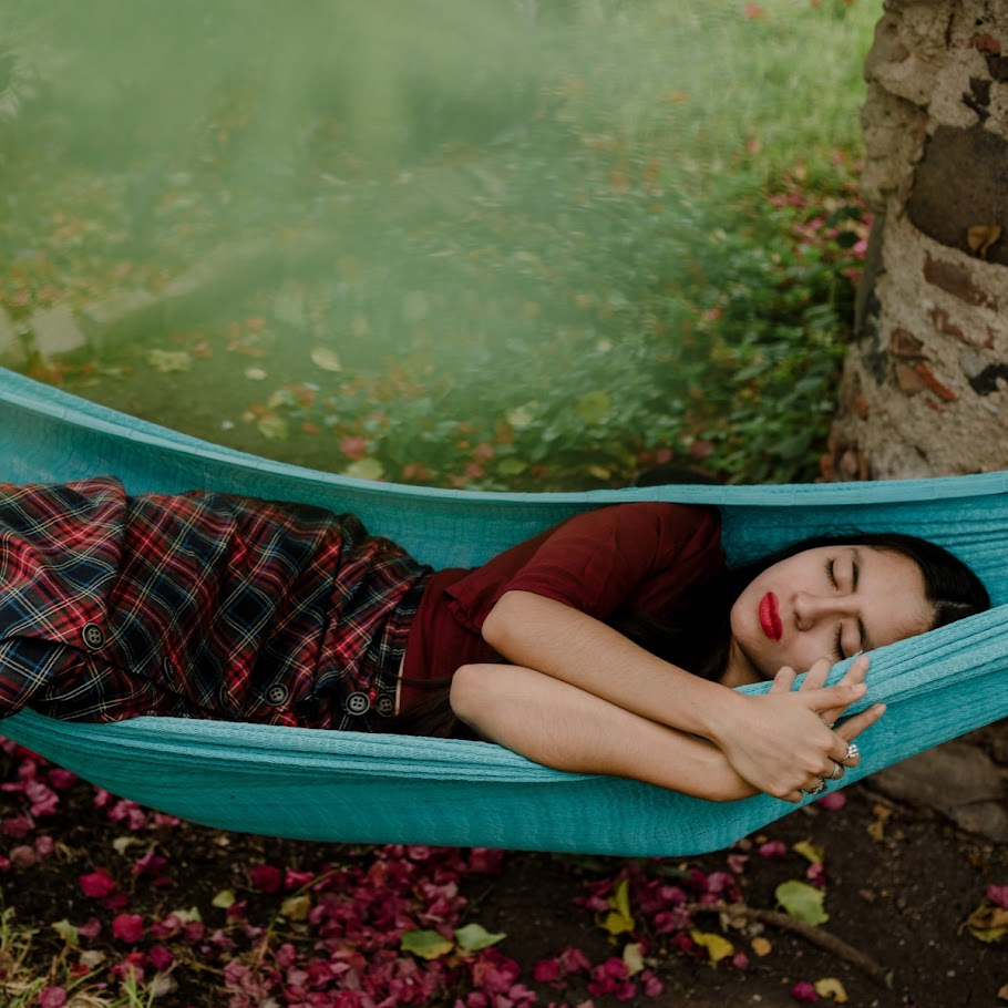 Woman sleeping on blue hammock outdoors surrounded by greenery.