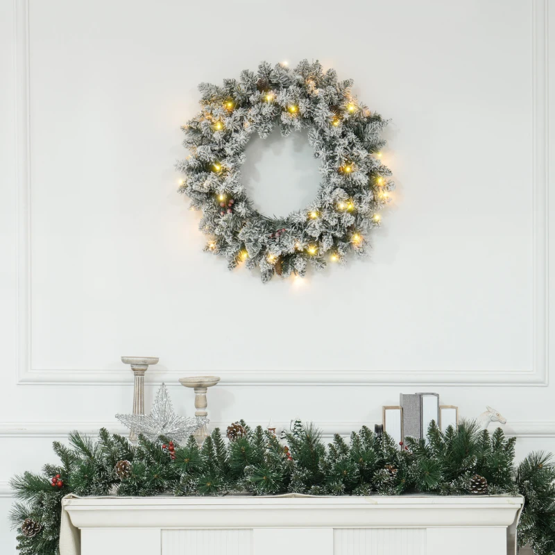 Lit Christmas wreath with frosted garland on white mantelpiece.