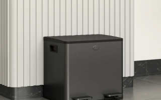 Black dual-pedal garbage bin placed neatly against a wall.