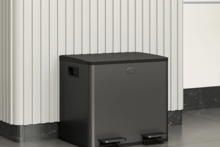 Black dual-pedal garbage bin placed neatly against a wall.