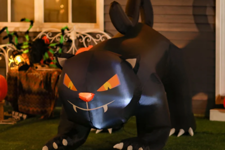 Black cat inflatable with glowing eyes on porch at night.