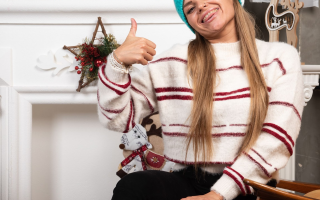 Woman in striped sweater smiling near decorated Christmas mantel.