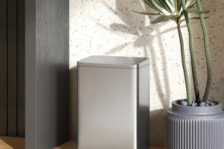 Modern stainless steel trash bin beside indoor plant.