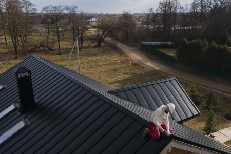 Roofer working on black metal roof of a house