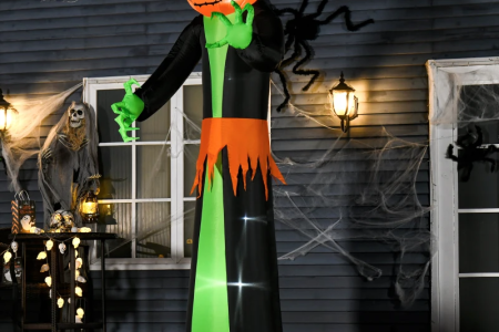 Giant inflatable pumpkin-head figure glowing in decorated yard with spider webs.