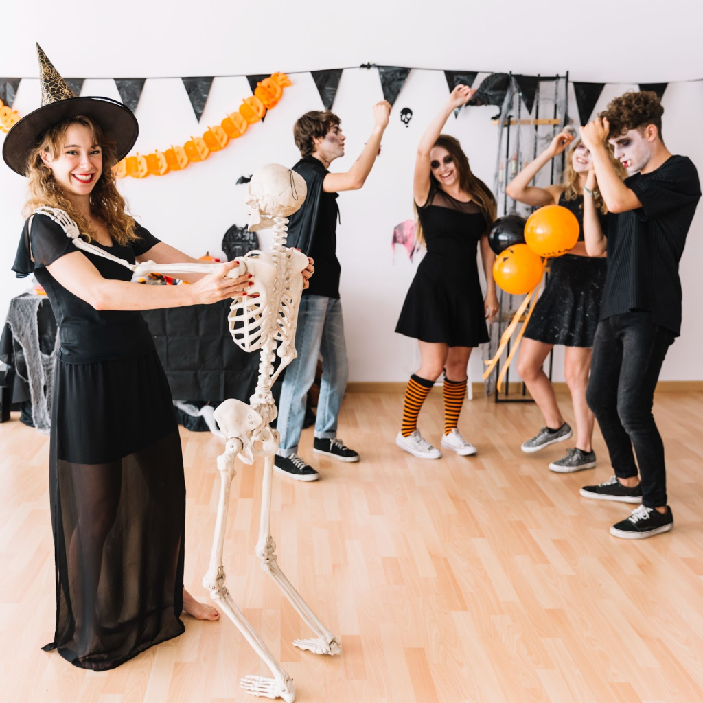 Teens in costumes dancing at a festive indoor Halloween party with balloons and banners.