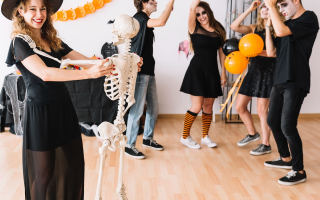 Teens in costumes dancing at a festive indoor Halloween party with balloons and banners.