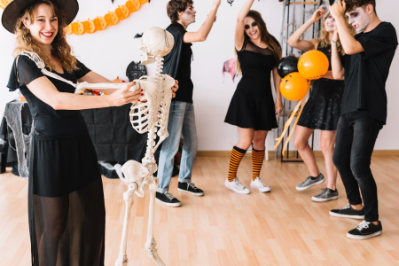 Teens in costumes dancing at a festive indoor Halloween party with balloons and banners.