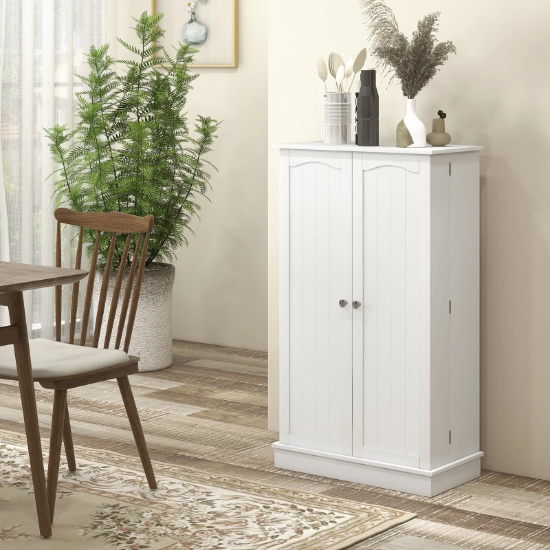 White pantry cabinet with double doors, decorated top, placed beside dining table and indoor plant.