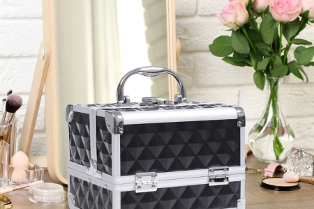 Black diamond-textured makeup train case on vanity beside mirror, flowers, and brushes.