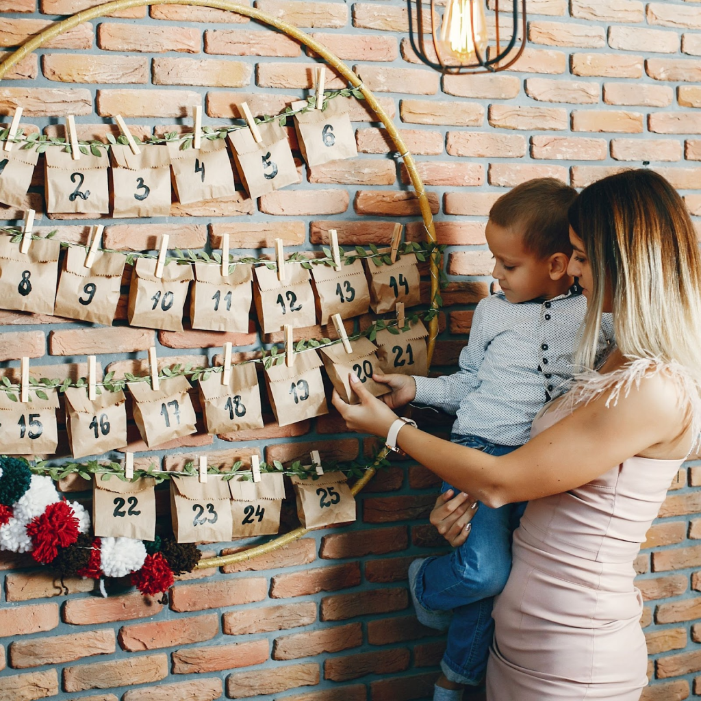 Mother and child opening DIY paper bag advent calendar on wall.