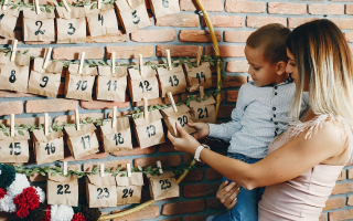 Mother and child opening DIY paper bag advent calendar on wall.