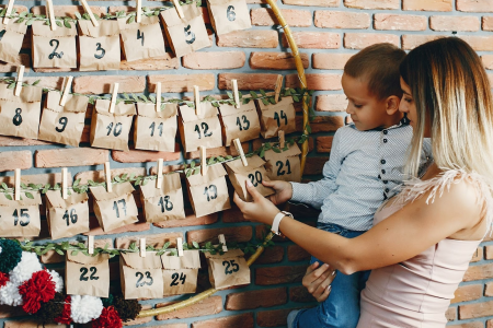Mother and child opening DIY paper bag advent calendar on wall.