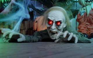 Crawling zombie with glowing red eyes on wooden floor Halloween setup.