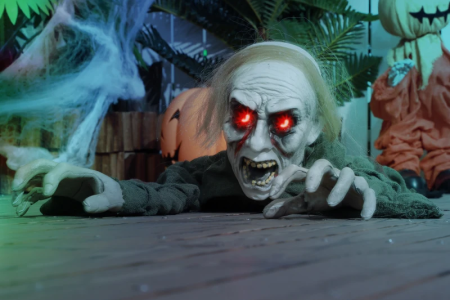 Crawling zombie with glowing red eyes on wooden floor Halloween setup.
