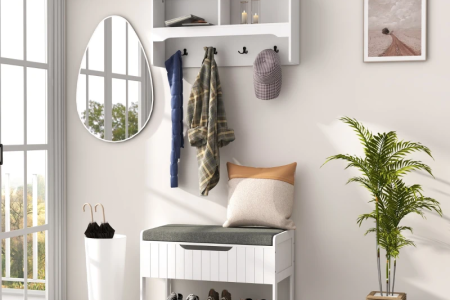 White hall tree with hooks, storage bench, mirror, and indoor plant in bright entryway.