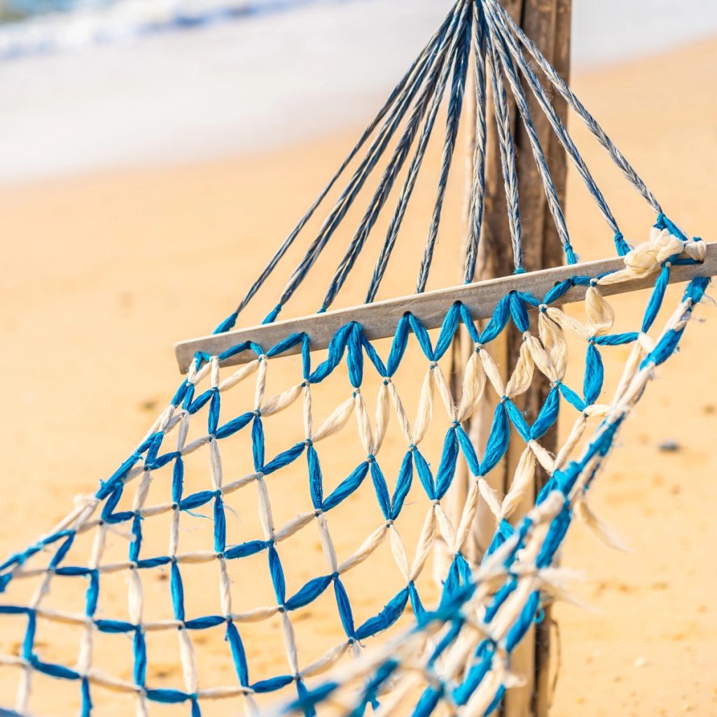 Blue and white rope hammock close-up on sandy beach background.