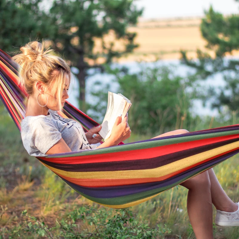 Woman relaxing and reading in colorful striped Brazilian hammock outdoors.