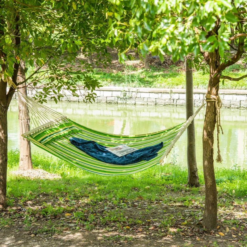 Green camping hammock with metal stand set up in forest campsite.
