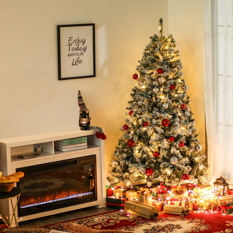 Snow-flocked Christmas tree decorated with red and gold ornaments beside fireplace