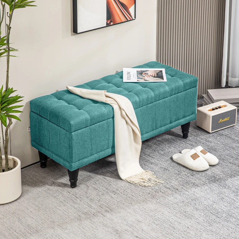 Green linen storage ottoman beside bed with magazine and plant
