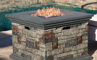 Stone gas fire pit with glowing flames beside pool