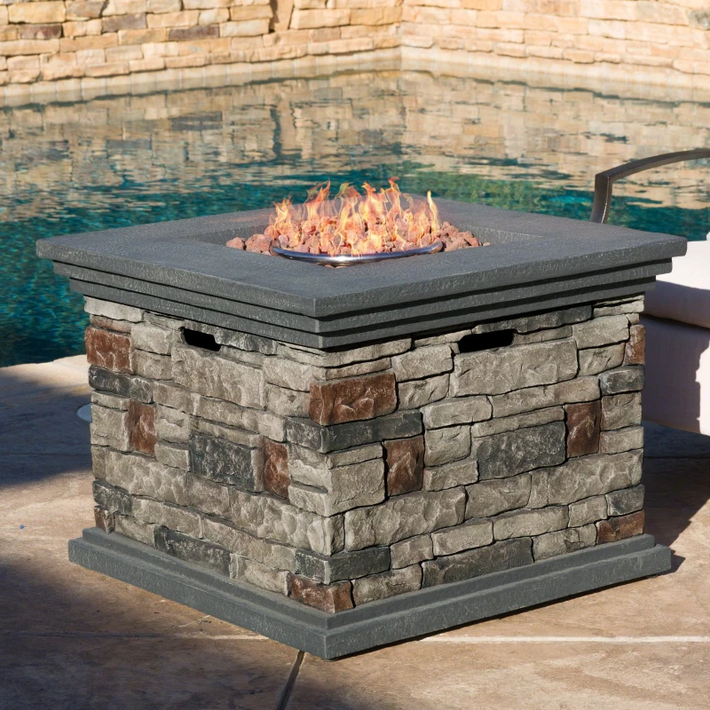 Stone gas fire pit with glowing flames beside pool