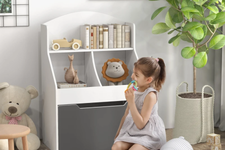 Little girl sitting near white and gray kids bookcase with books, toys, and decor in a cozy playroom setting.