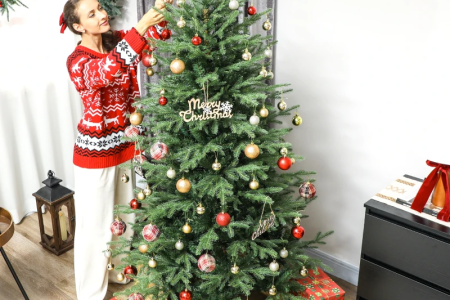 Woman decorating a Christmas tree with ornaments in cozy living room.