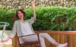 Woman enjoying a wooden porch rocking chair outdoors on patio.