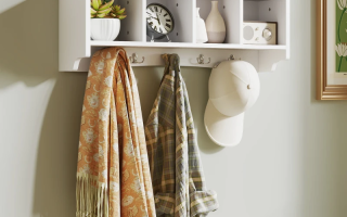 White wall-mounted coat rack with four shelves and hooks holding scarves, shirts, and a cap.