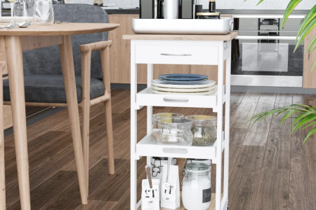 White-painted kitchen cart styled with plates, jars, and bottles in a modern kitchen.